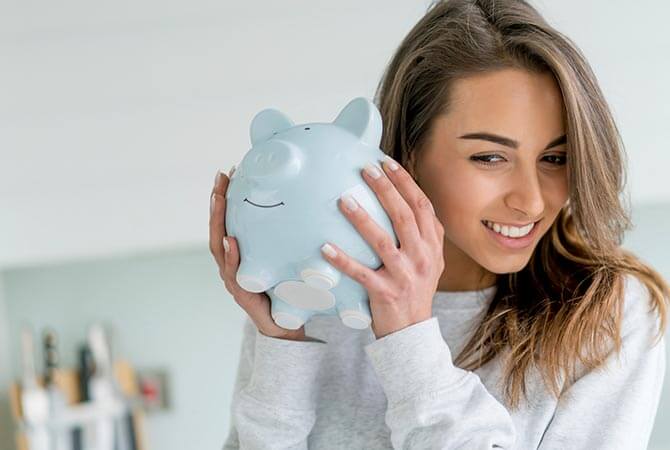 Young adult woman holding a piggy bank to her ear