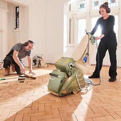 Husband and wife redoing hardwood floors with rented equipment